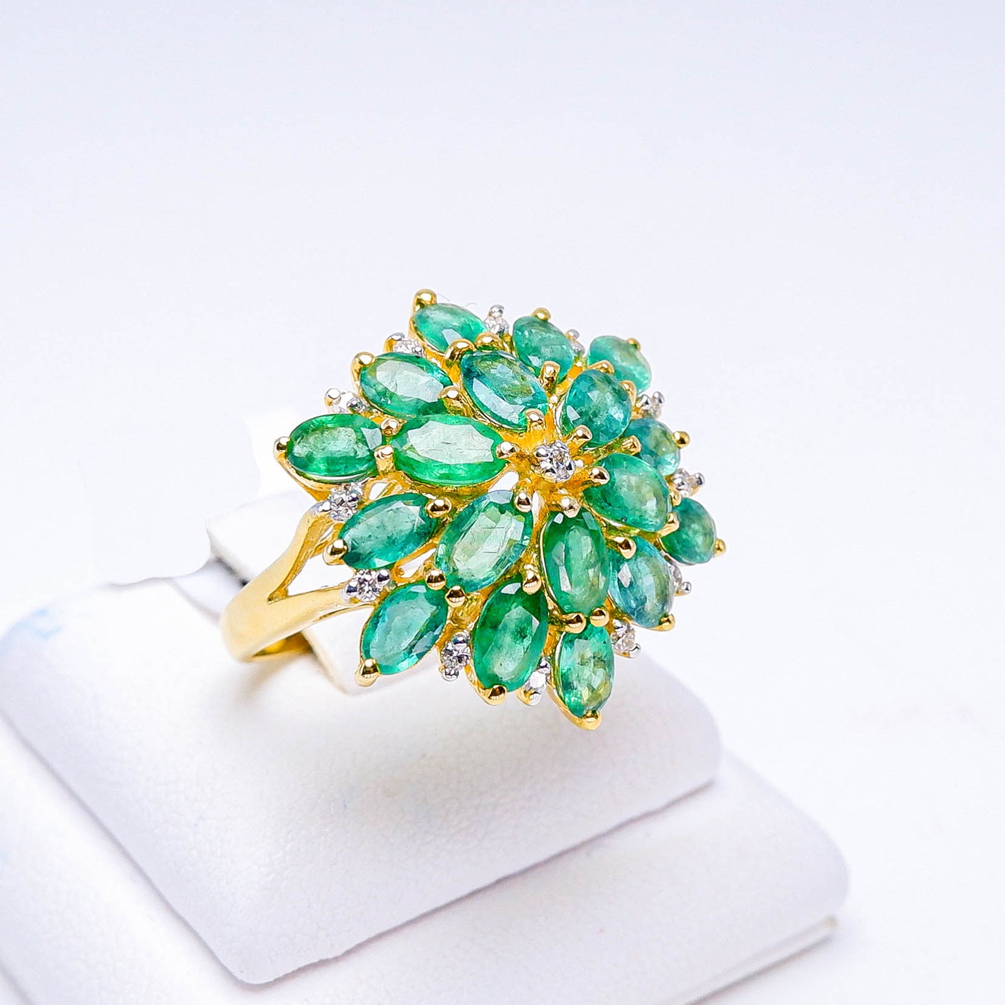 Gold ring with cluster of marquise-cut green gemstones and small diamonds on white display