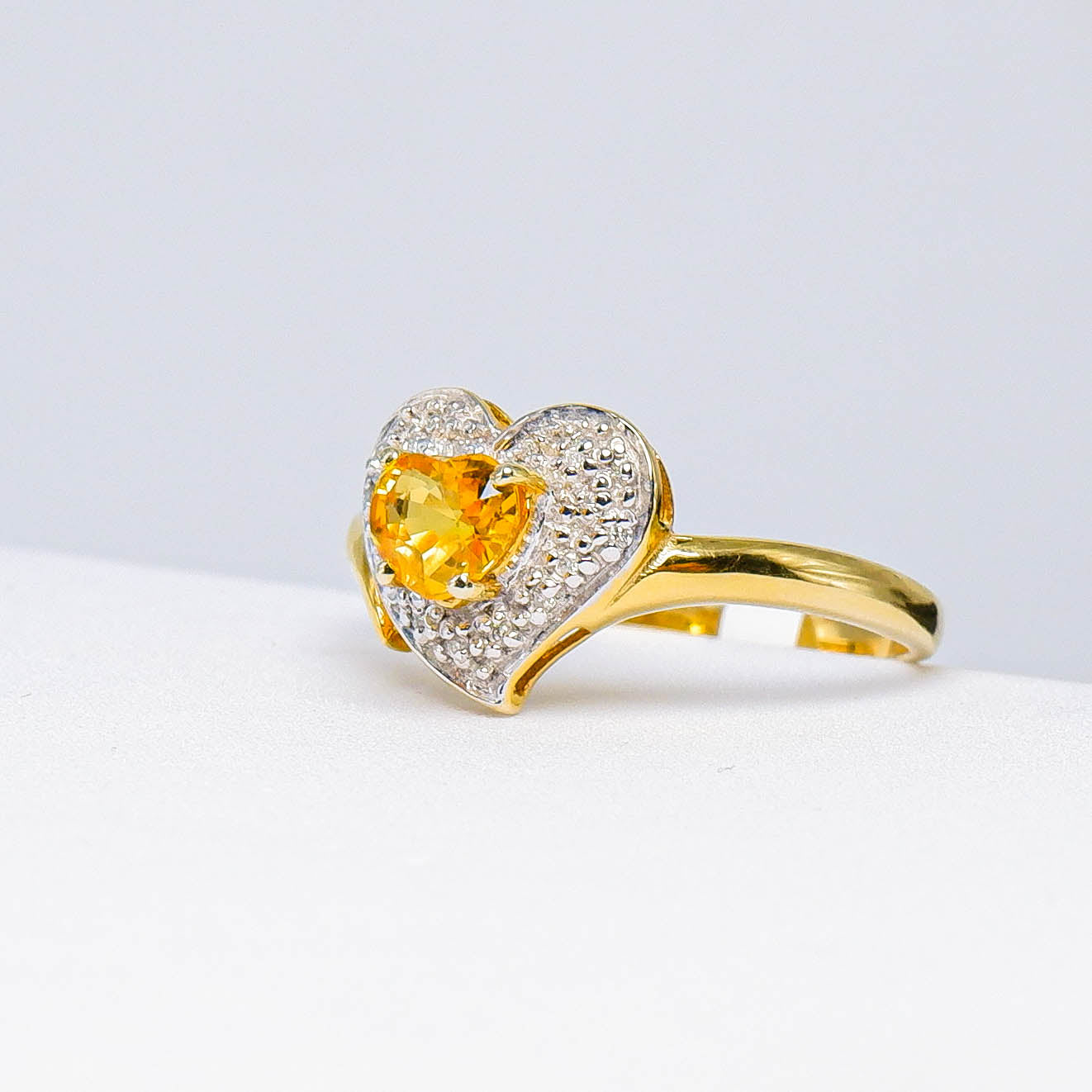 Heart-shaped yellow gemstone gold ring with small diamonds on a white background