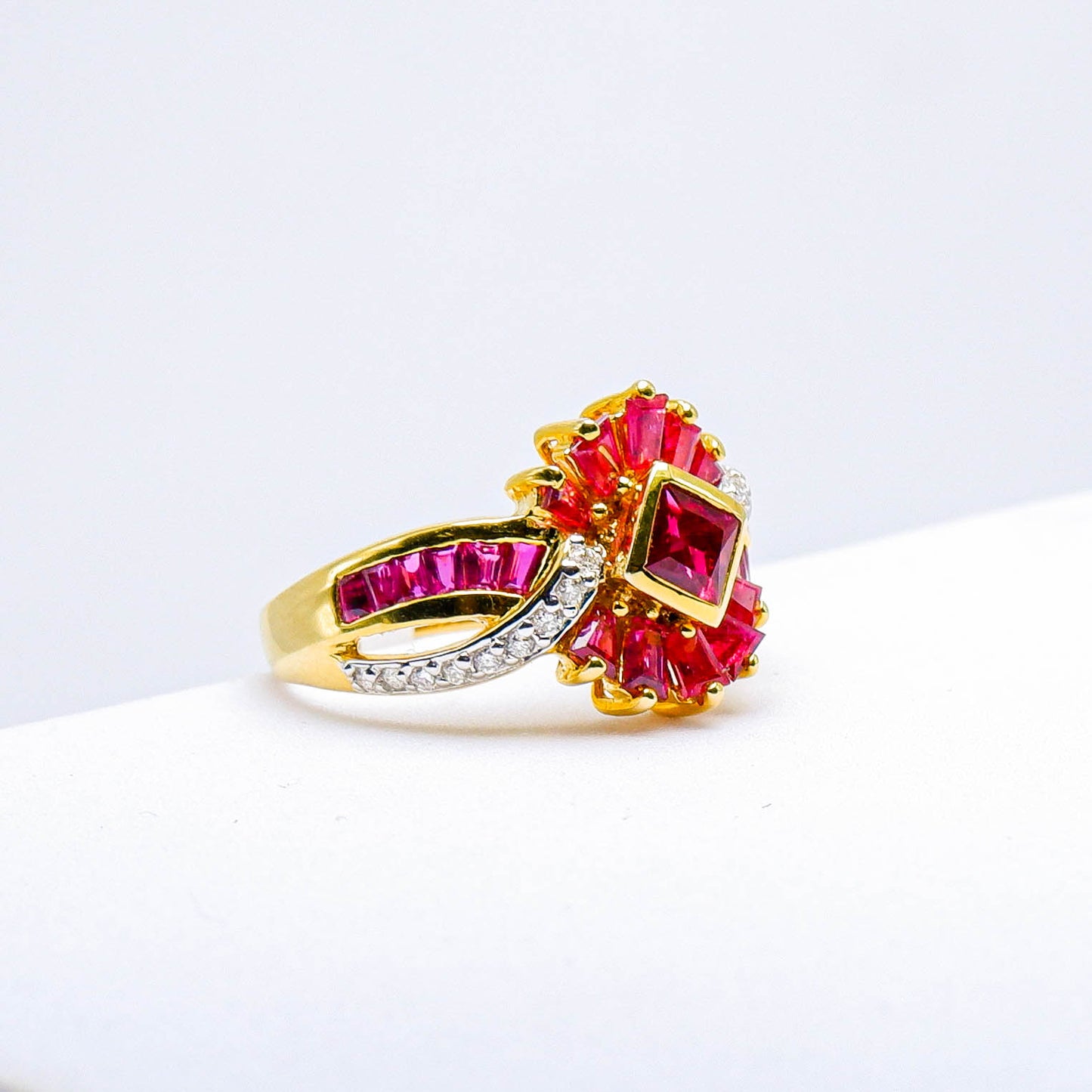 Gold ring with square and baguette-cut red gemstones and small white accents on a white background.