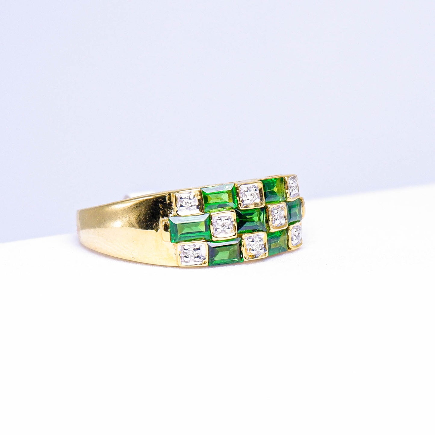 Gold ring with square green gemstones and white stones set in a geometric pattern