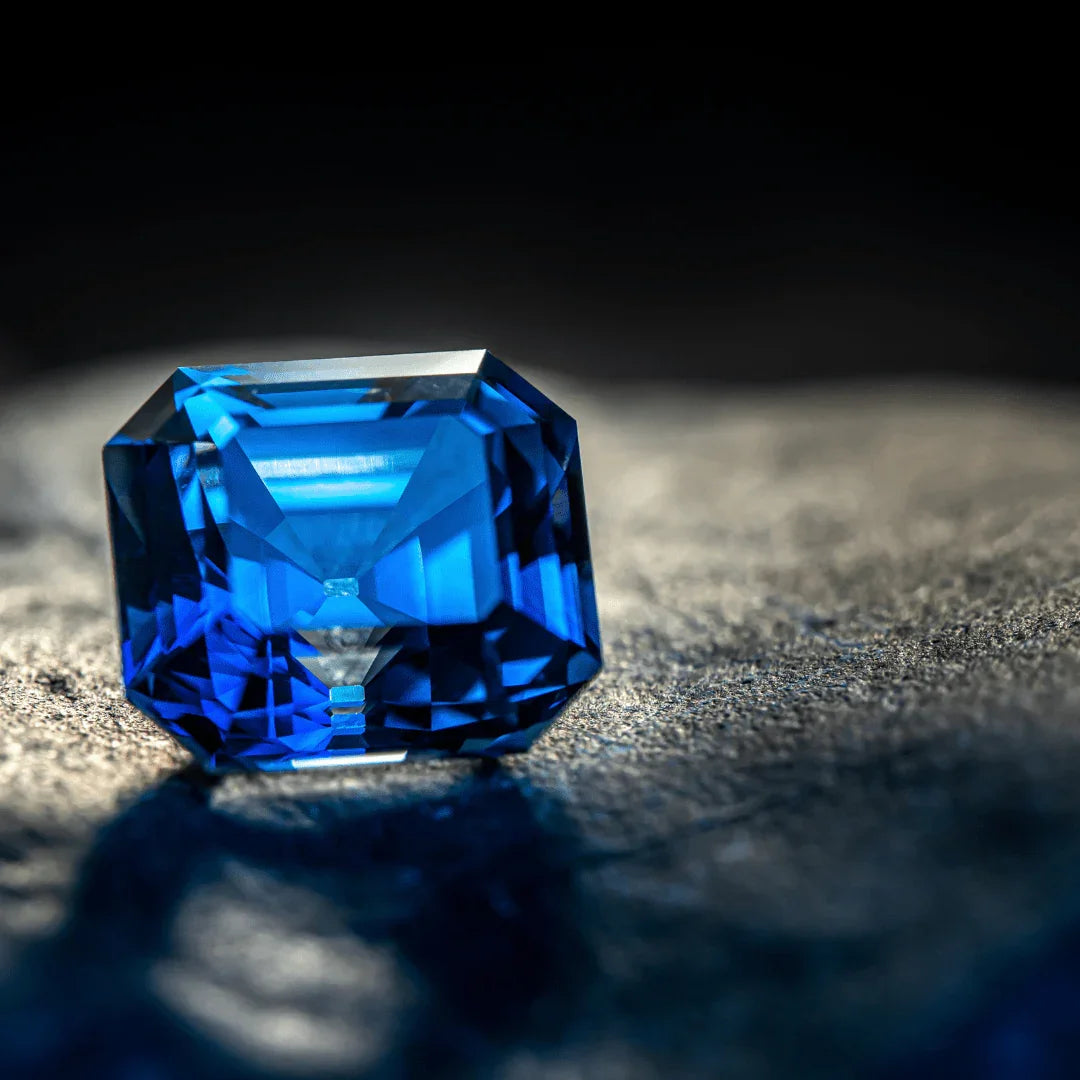 Emerald-cut blue sapphire gemstone with vivid color on a textured surface, close-up