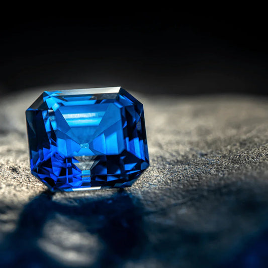 Emerald-cut blue sapphire gemstone with vivid color on a textured surface, close-up
