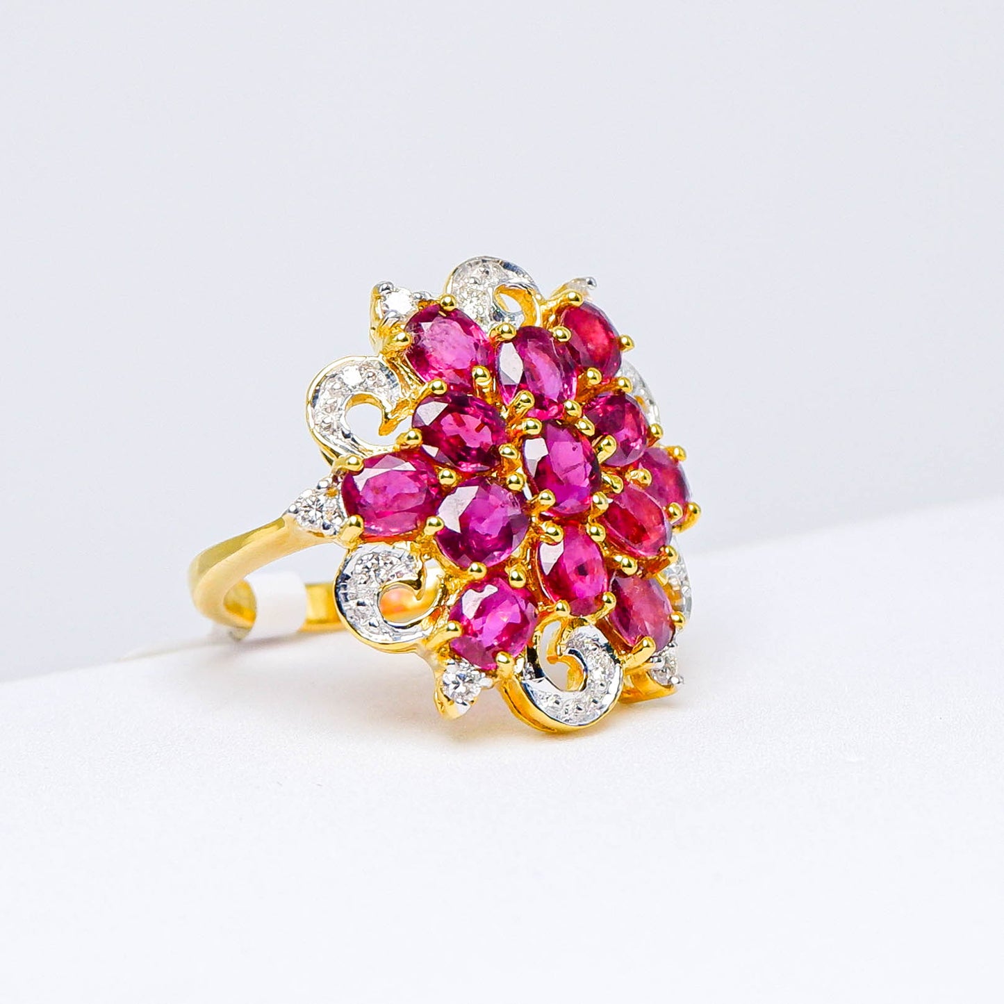 Gold ring with floral cluster of natural red gemstones and white accent stones on white background