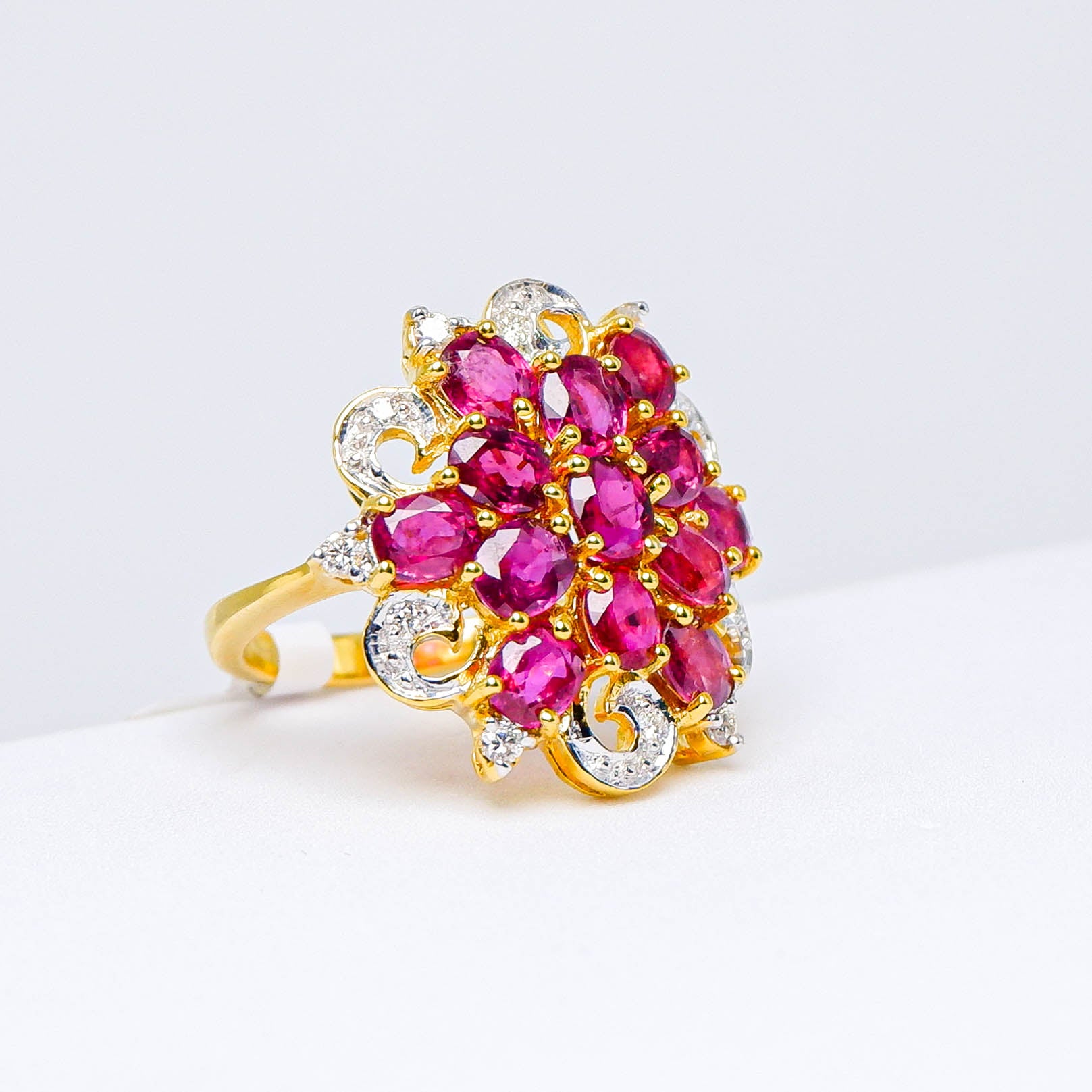 Gold ring with floral cluster of natural red gemstones and white accent stones on white background