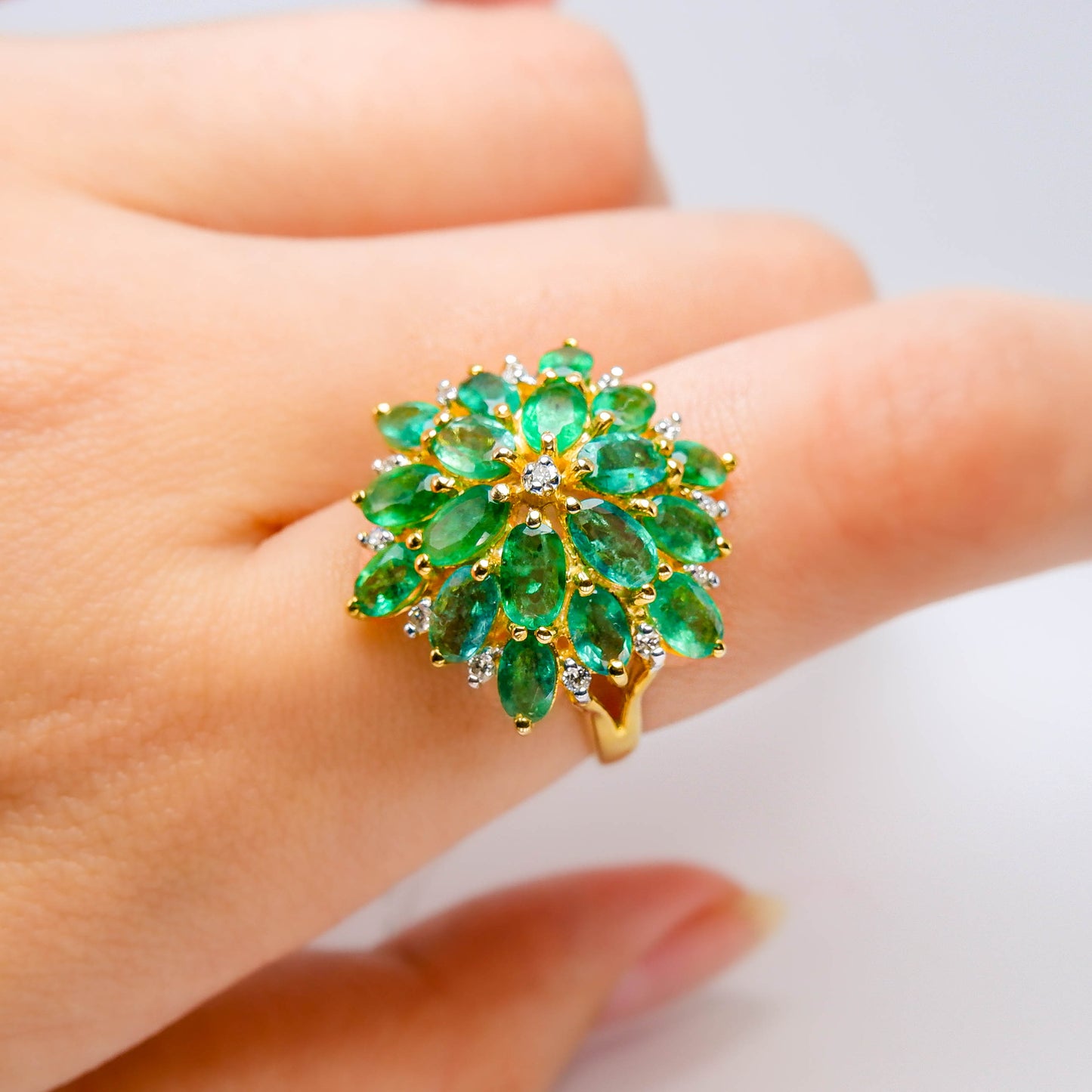 Gold ring with natural green emerald gemstones and diamonds in floral design on hand