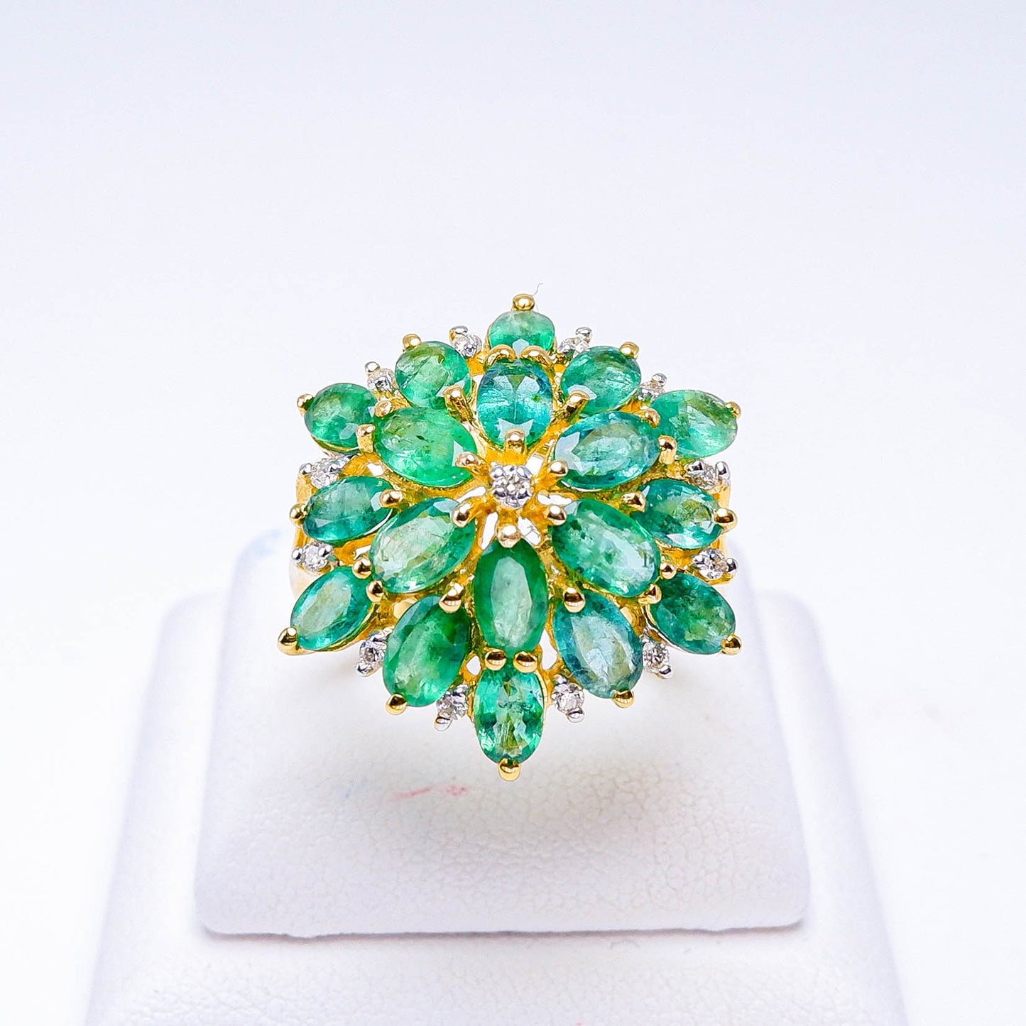 Gold ring with marquise-cut green gemstones and diamonds in a floral cluster design on display stand
