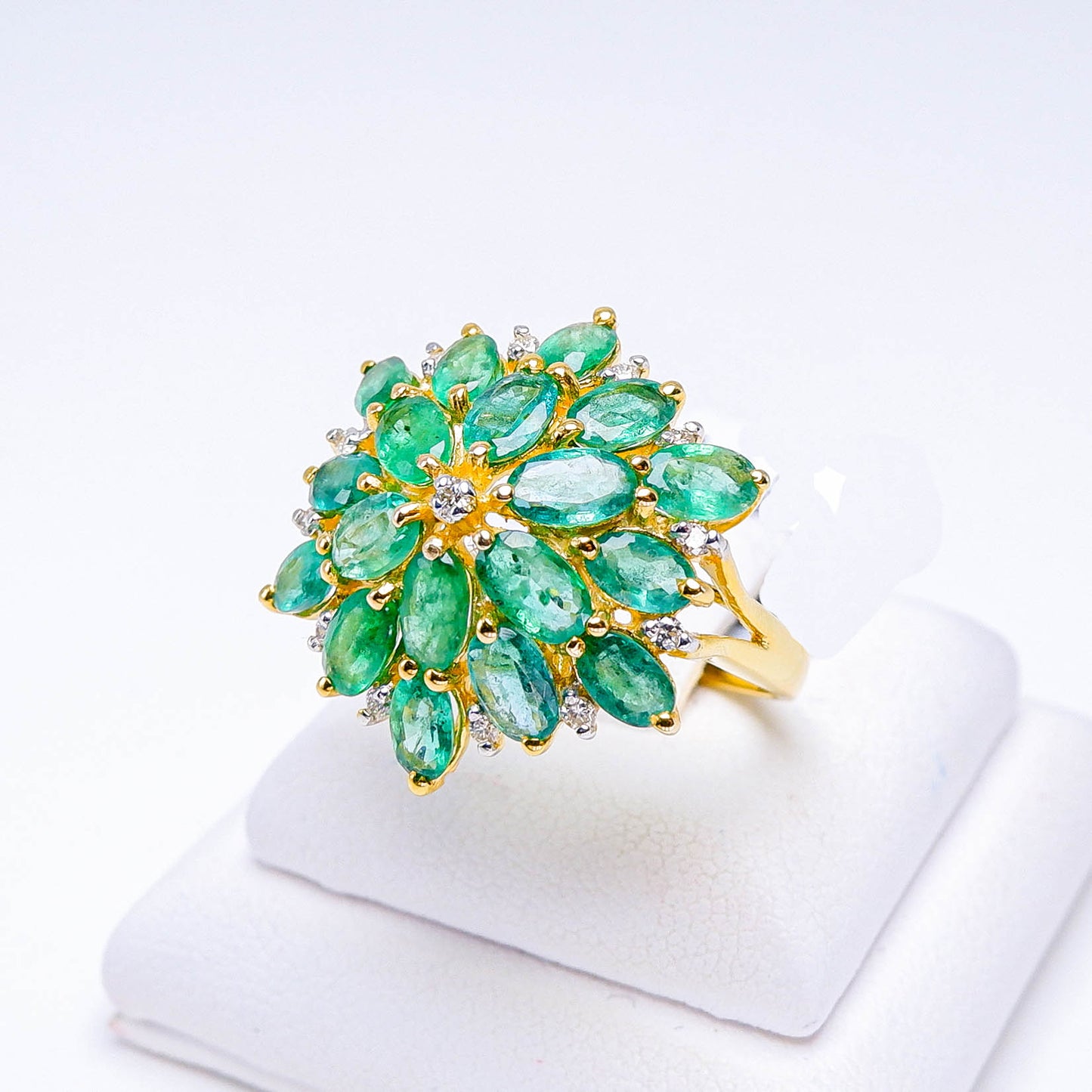 Gold ring with marquise-cut green gemstones and small diamonds in a floral cluster design on display.