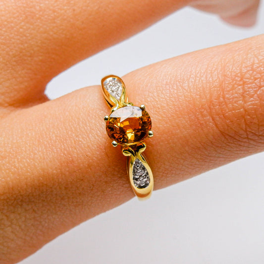 Yellow gold ring with round orange gemstone and small diamonds on finger