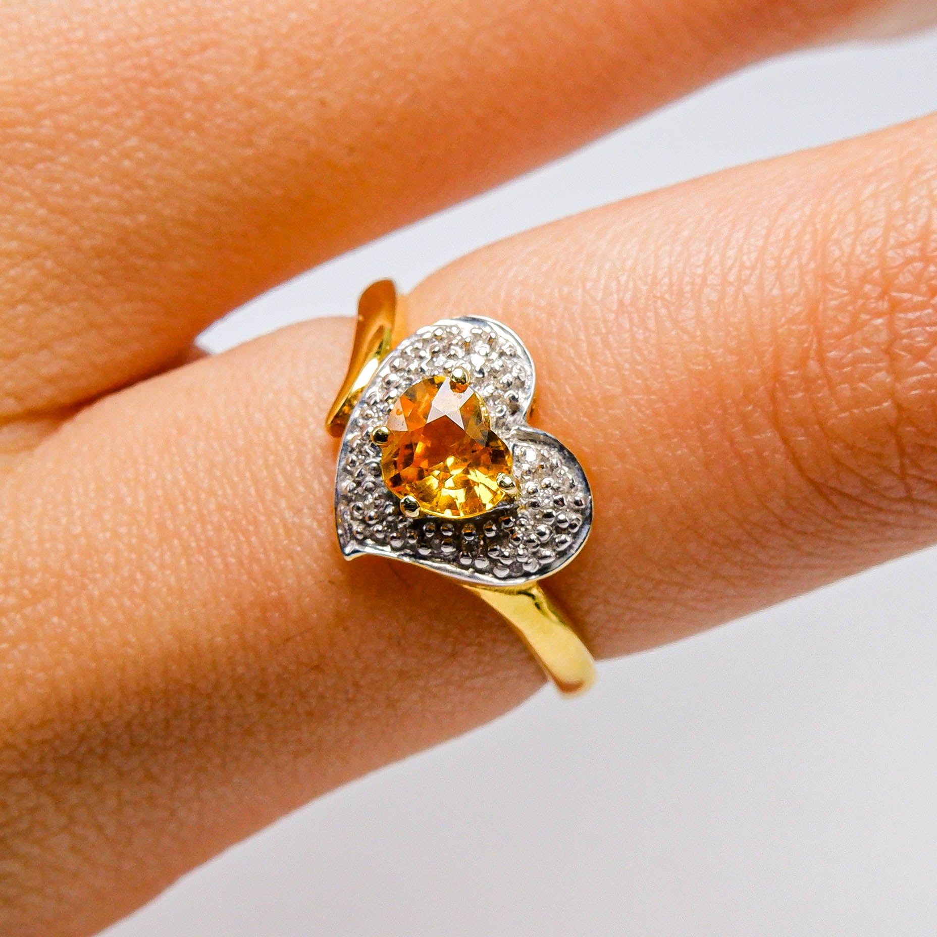 Gold heart-shaped ring with yellow gemstone and diamond accents on finger