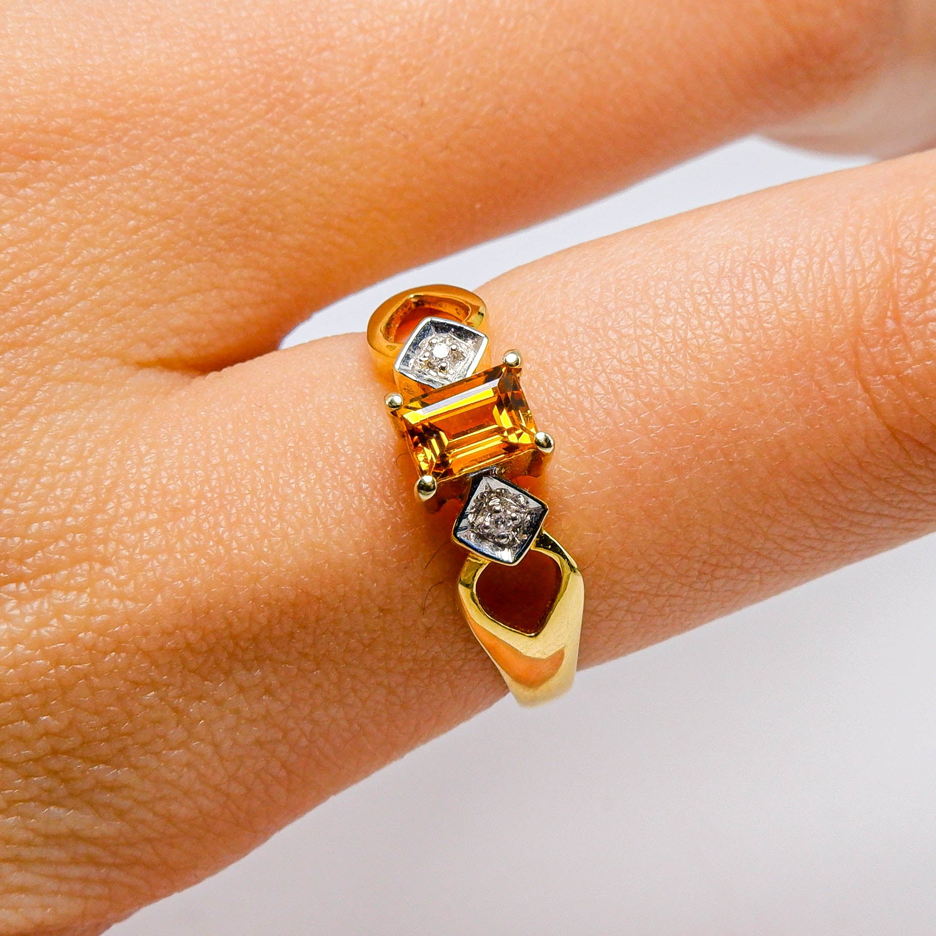 Gold ring with rectangular yellow gemstone and small diamonds on finger