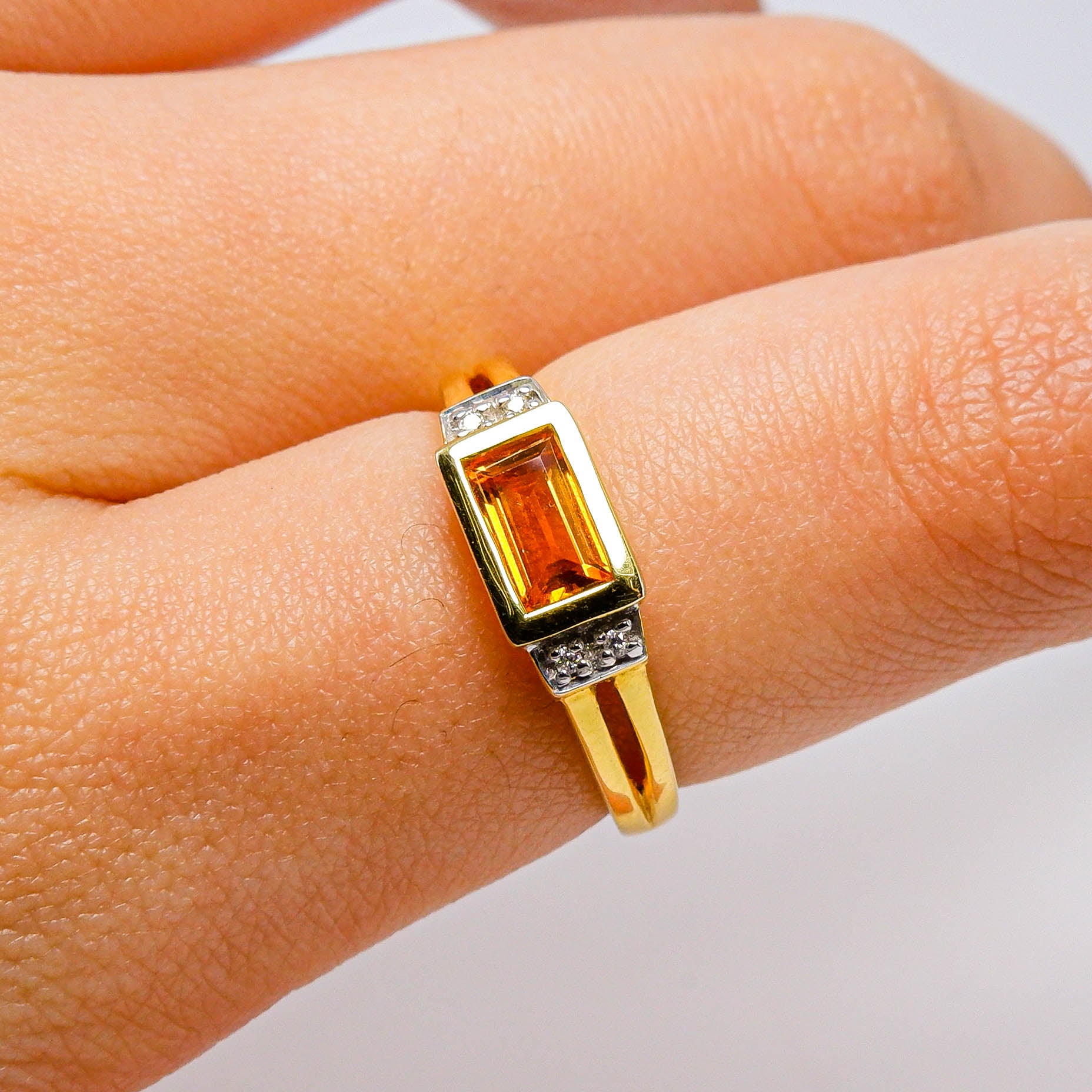 Gold ring with rectangular orange gemstone and small white accent stones on finger