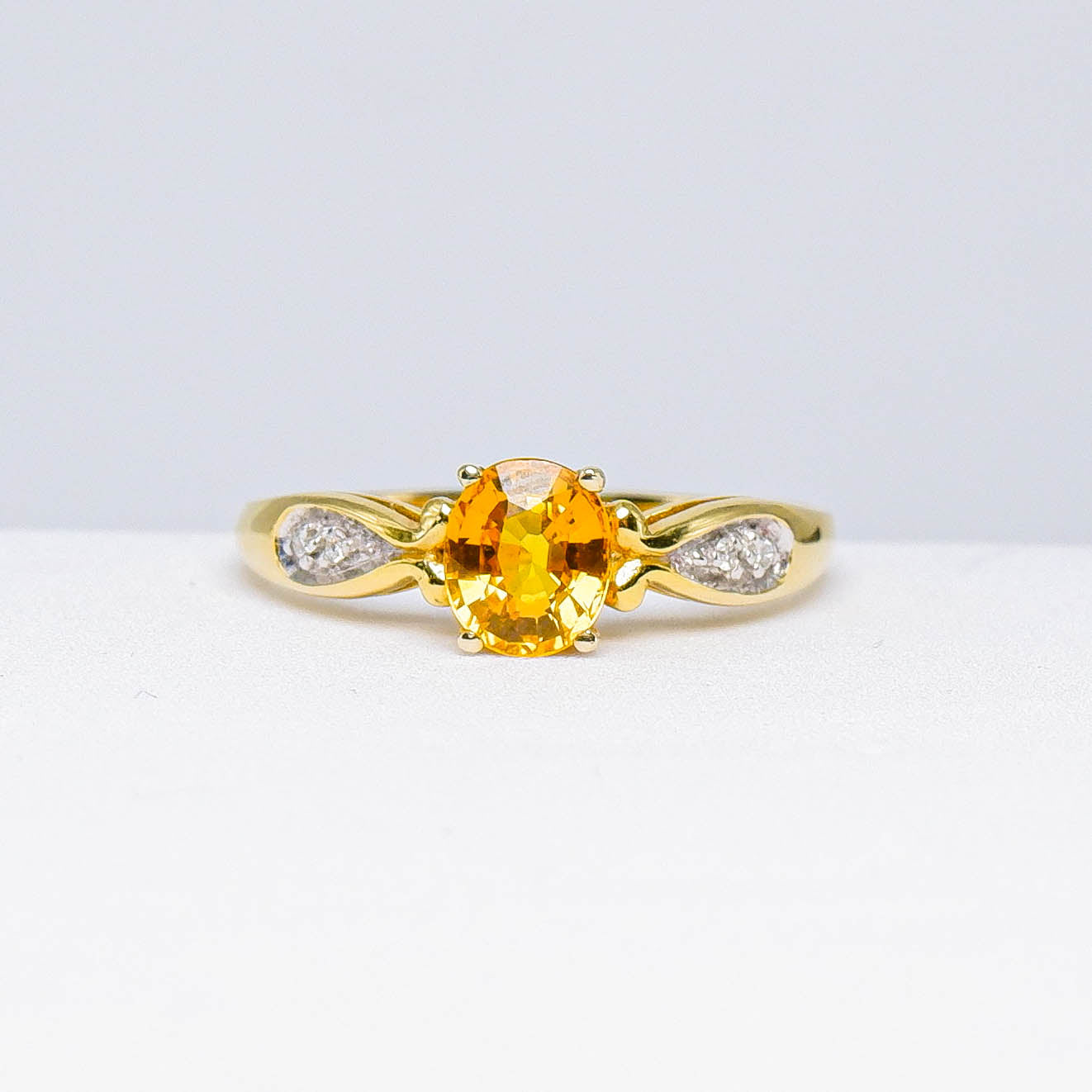 Gold ring with oval yellow gemstone and side diamond accents on white background