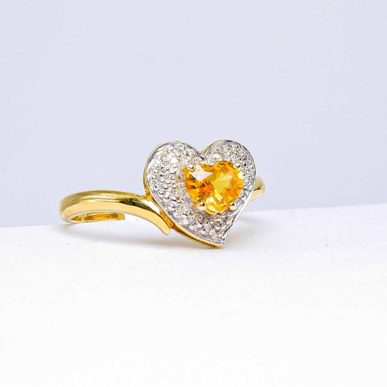 Heart-shaped yellow gemstone and diamond ring with gold band on white background