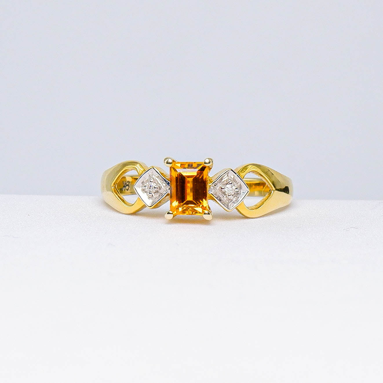 Gold ring with rectangular orange gemstone and two diamond accents on white background