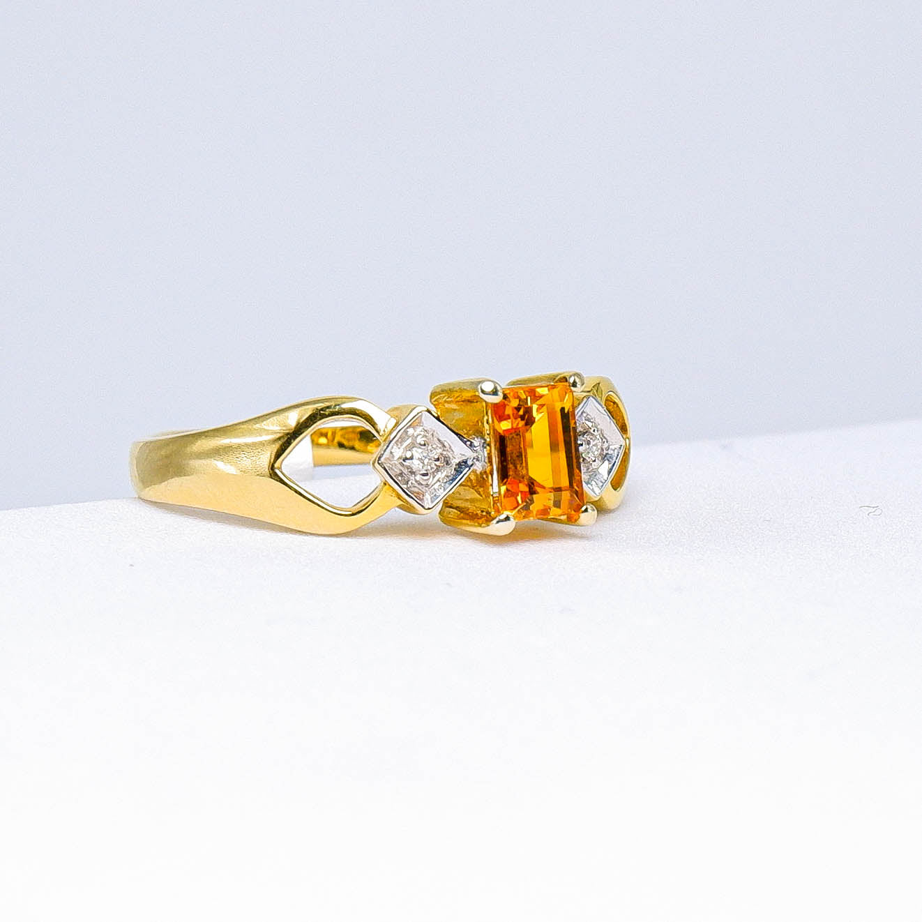 Gold ring with rectangular orange gemstone and diamond accents on white background