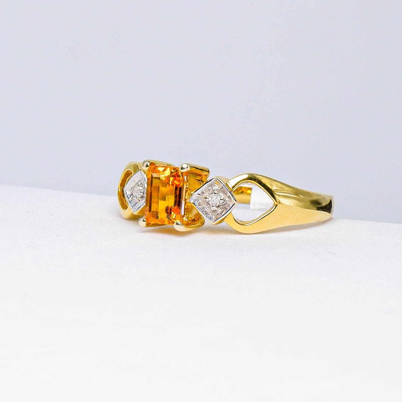 Gold ring with rectangular yellow sapphire and diamond accents on white background