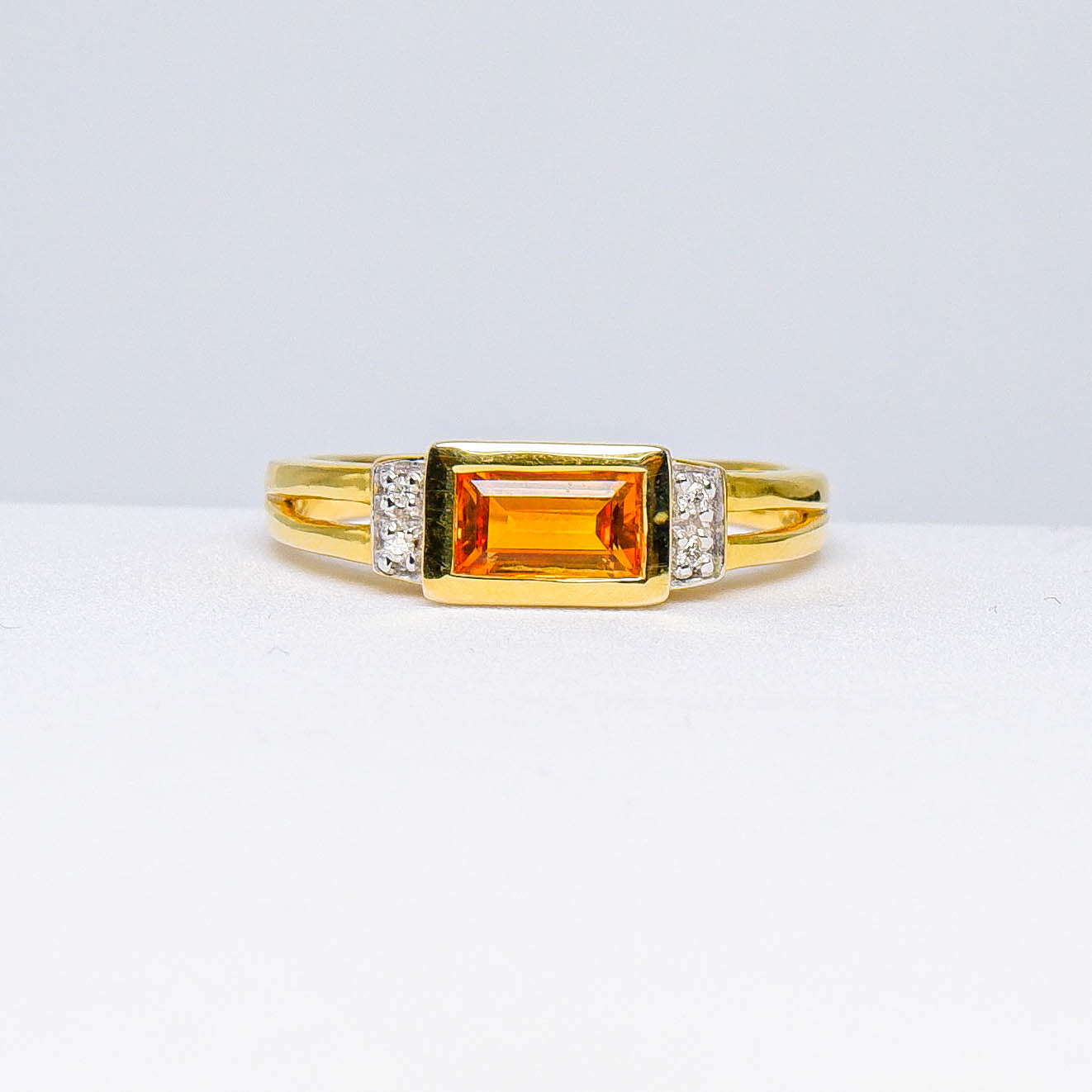 Gold ring with rectangular orange gemstone and diamond accents on white surface