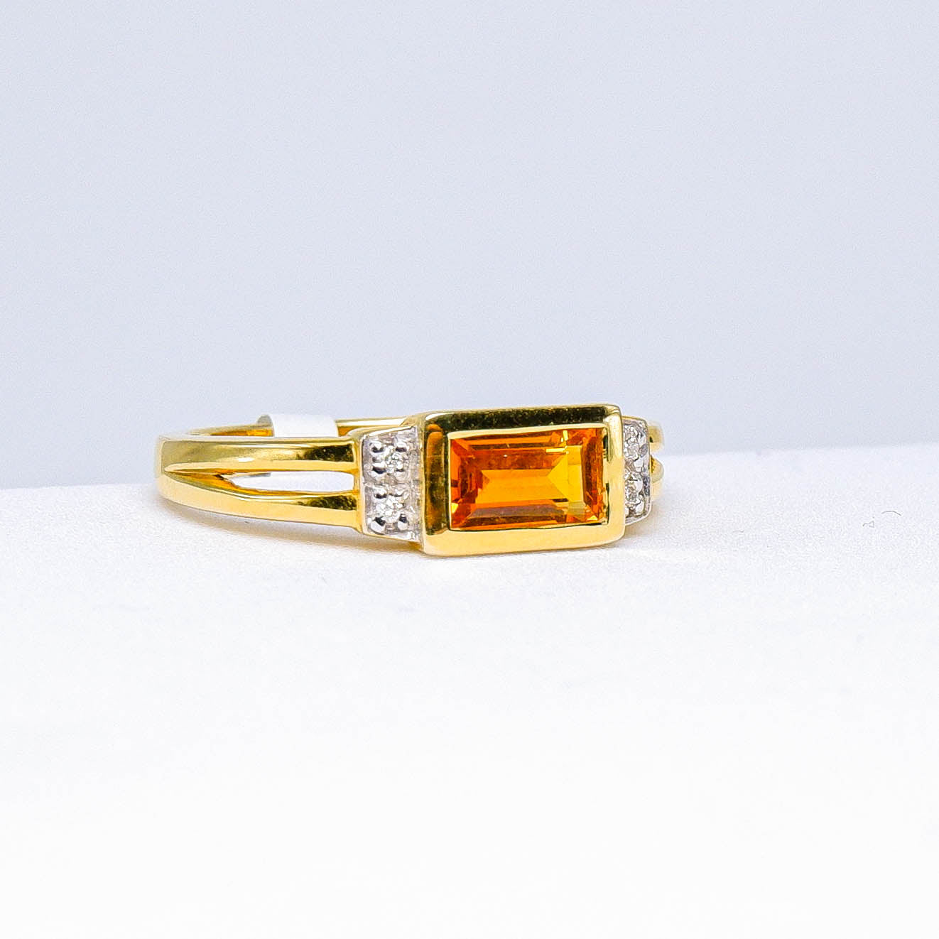 gold ring with rectangular orange gemstone and small clear accent stones on white background