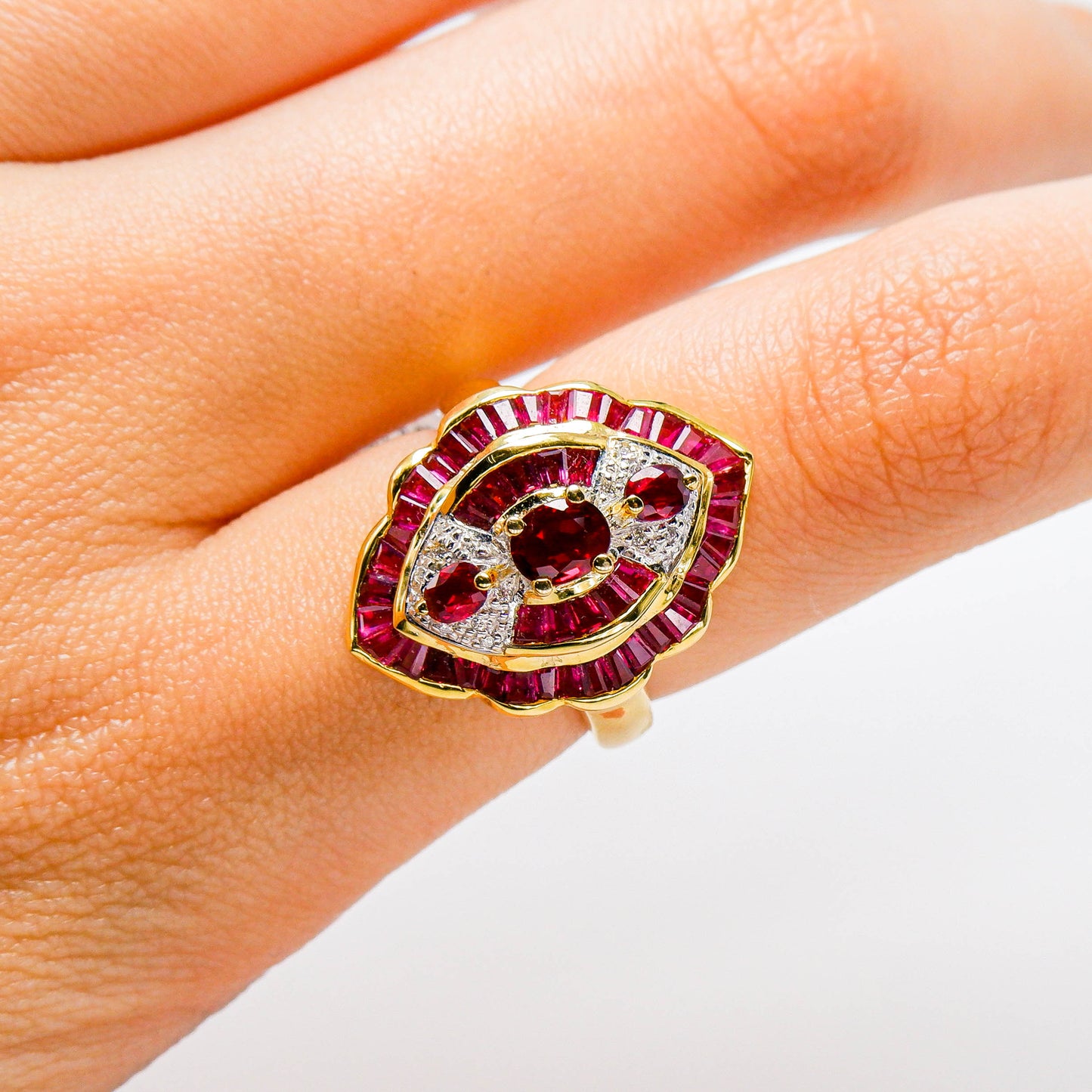 Gold ring with red gemstones and diamonds in an eye shape on a person's finger