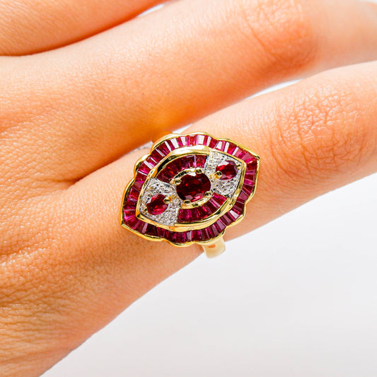 Gold ring with red gemstones and diamonds in an eye shape on a person's finger