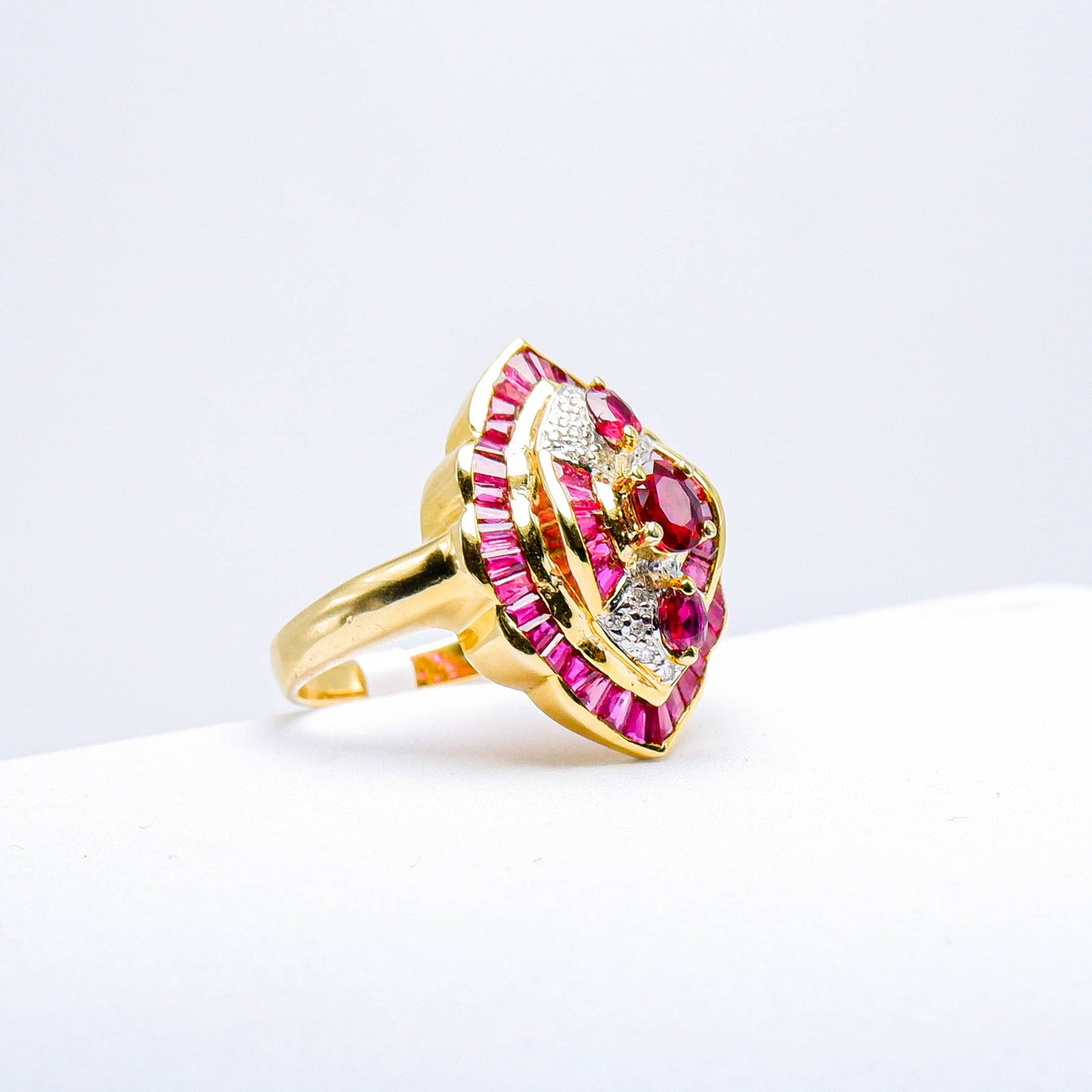 Gold ring with red gemstones and diamond accents on white background
