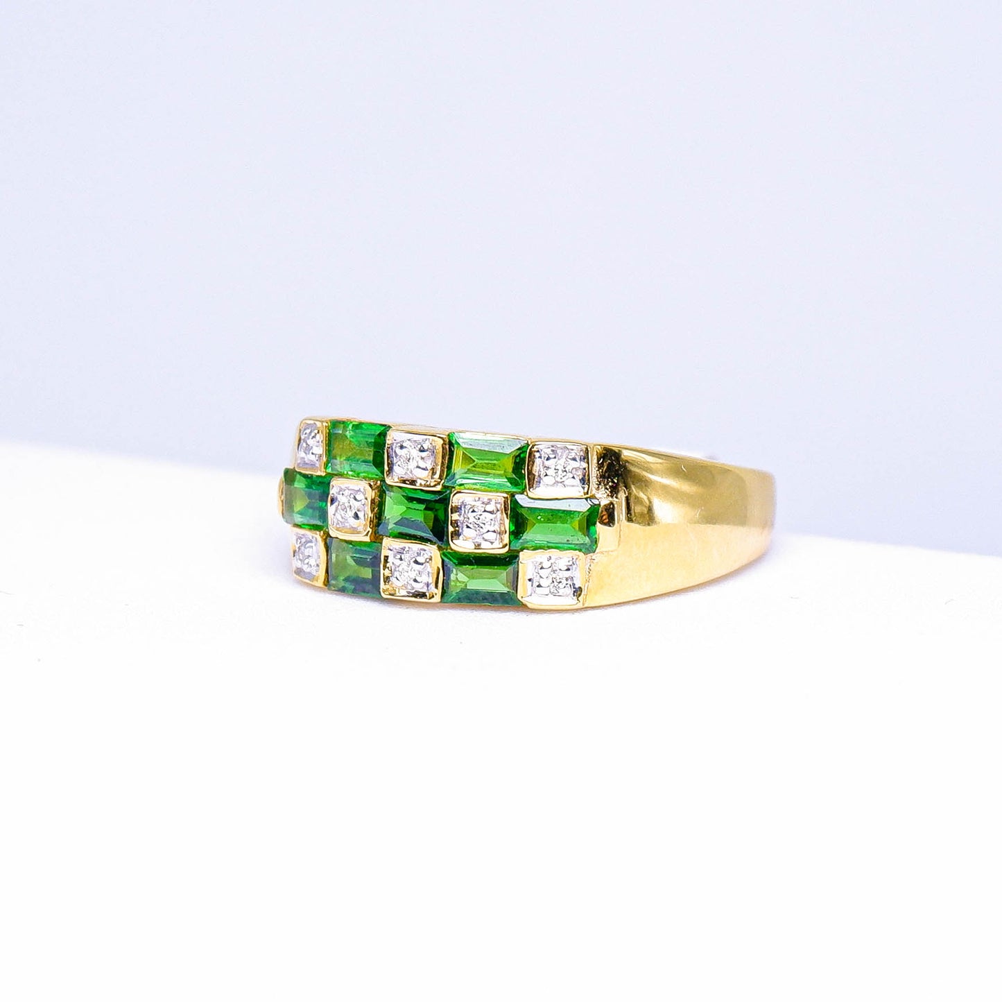 Gold ring with square green gemstones and clear stones in a geometric pattern on white background