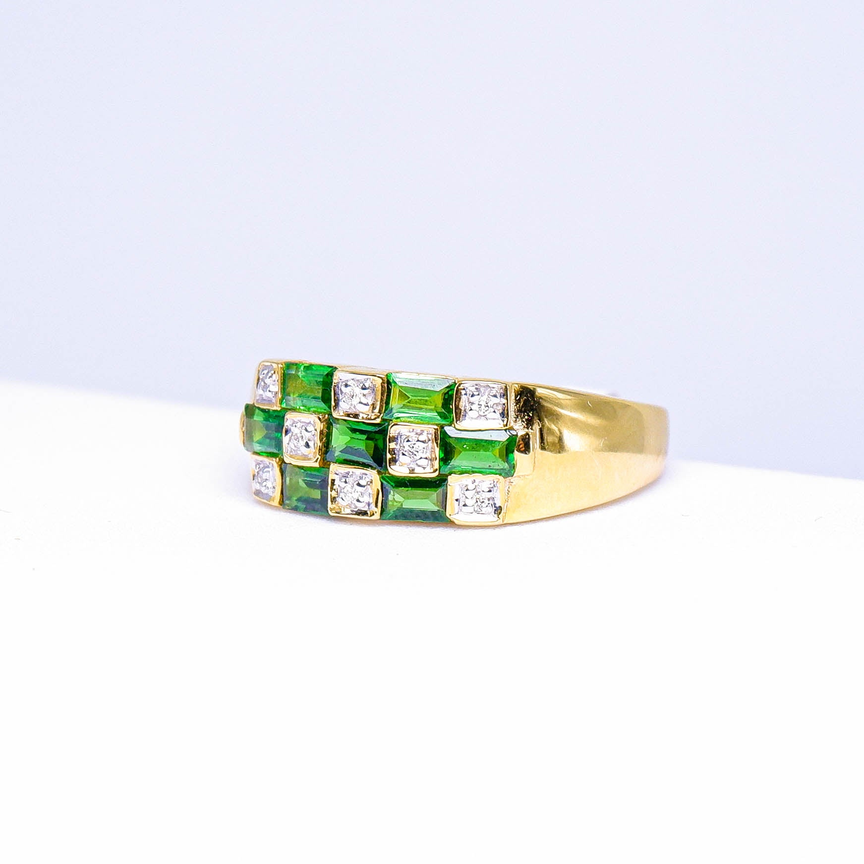 Gold ring with square green gemstones and clear stones in a geometric pattern on white background