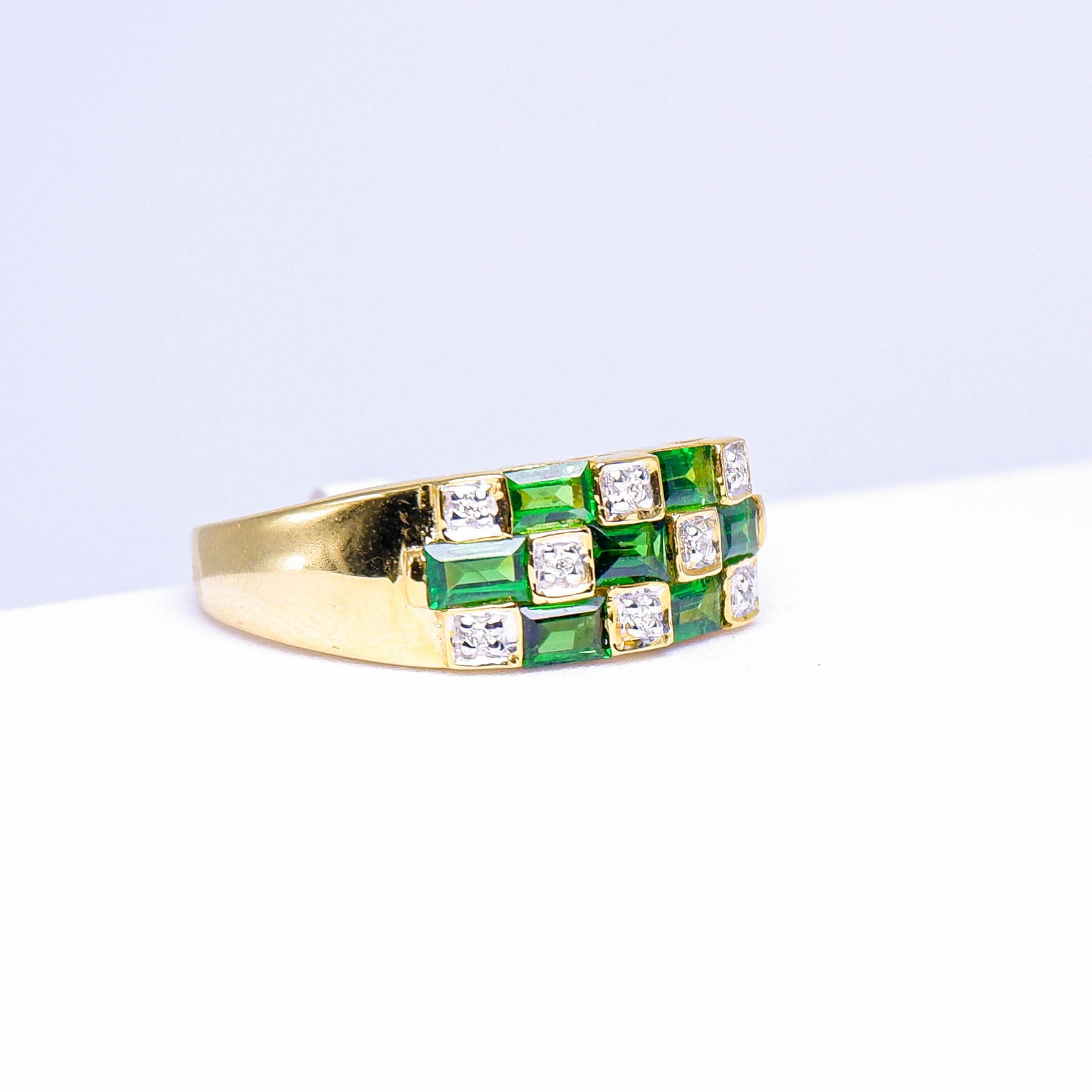Gold ring with square green gemstones and white stones set in a geometric pattern